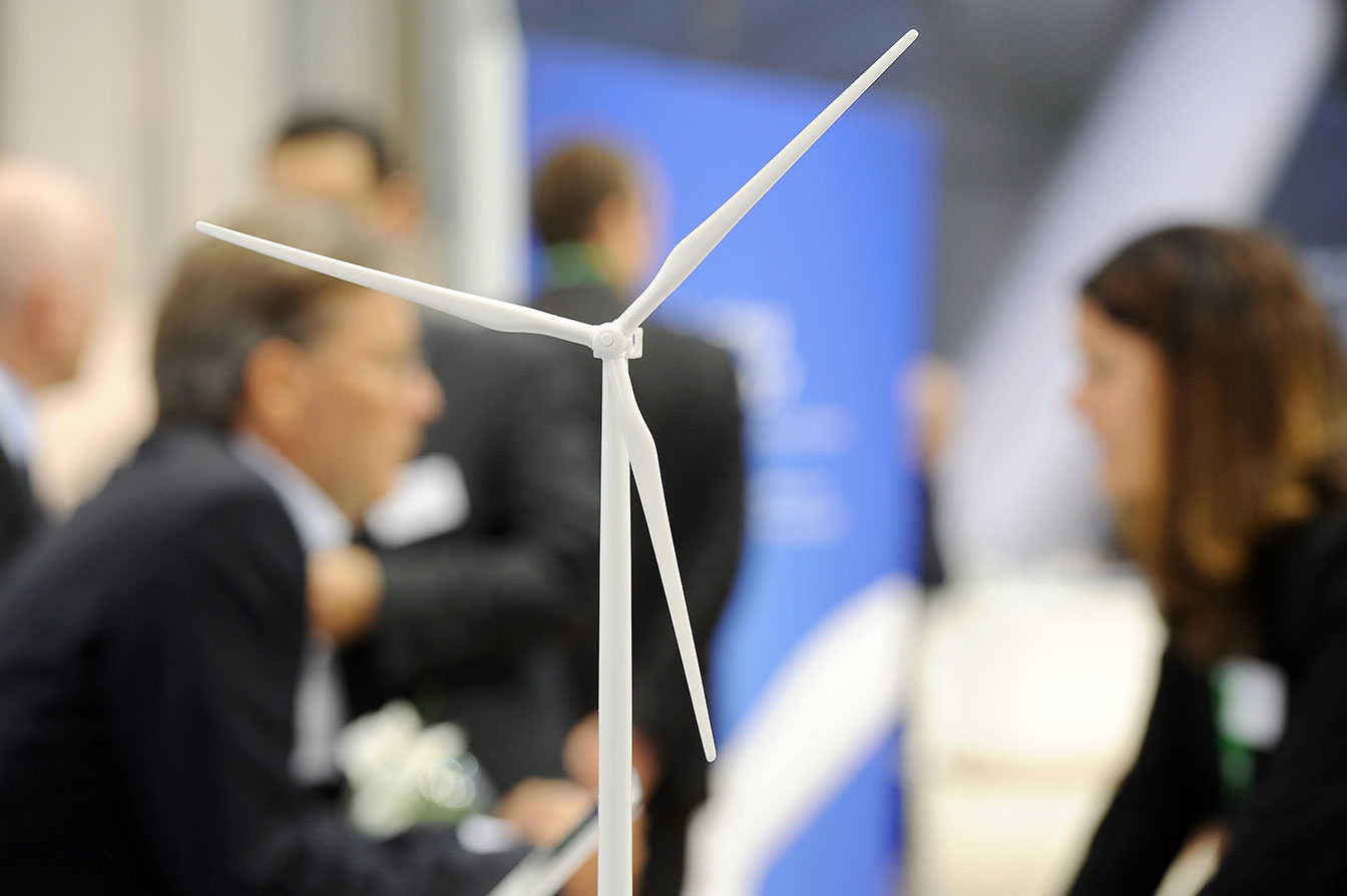 Kleines Modell eines Windrades auf der WindEnergy Hamburg, im Hintergrund Messebesucher im Gespräch